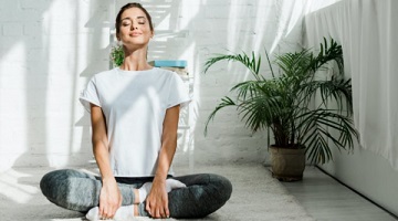 Pessoa sentada em posi&ccedil;&atilde;o de medita&ccedil;&atilde;o diante de uma janela com luz suave da manh&atilde;