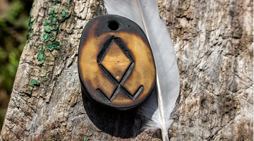 Pedra com a runa Othala gravada, ao lado de outras runas sobre um tecido escuro