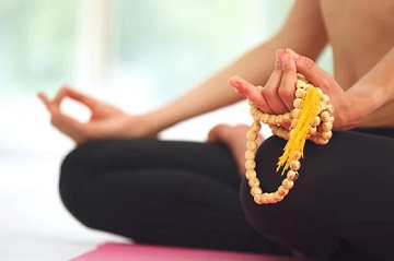 Pessoa meditando com contas de mala nas m&atilde;os, repetindo um mantra