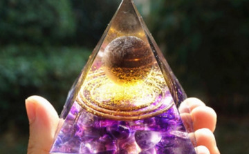 Pe&ccedil;a de orgonite em formato de pir&acirc;mide, com cristais de quartzo e lascas de metal vis&iacute;veis na resina