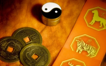 Tr&ecirc;s moedas chinesas antigas sobre um livro aberto com hexagramas, ao lado de varetas de bambu